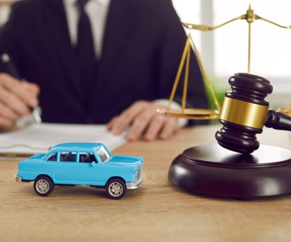 Voiture miniature bleue placée devant un marteau de juge et une balance de la justice, symbolisant le litige en vice caché automobile