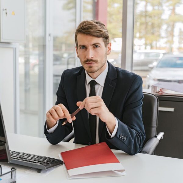 Conseiller automobile en costume assis à son bureau dans une concession, stylo à la main