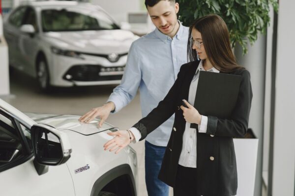 Conseillère automobile et client examinant ensemble un SUV hybride blanc en concession