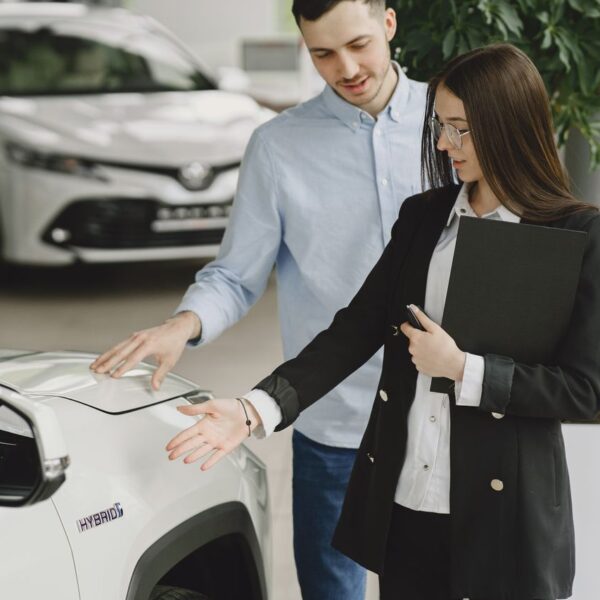 Conseillère automobile et client examinant ensemble un SUV hybride blanc en concession