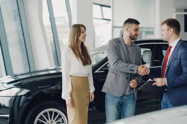 Couple achetant une voiture d’occasion en concession, poignée de main avec le vendeur
