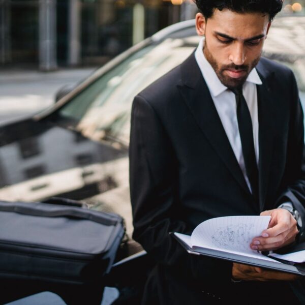 Homme en costume consultant des documents à côté d’une voiture noire